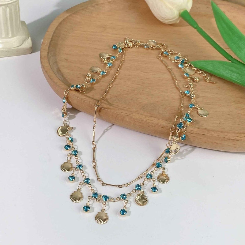 Ariana – Gold necklace with shells & blue crystals in boho beach style